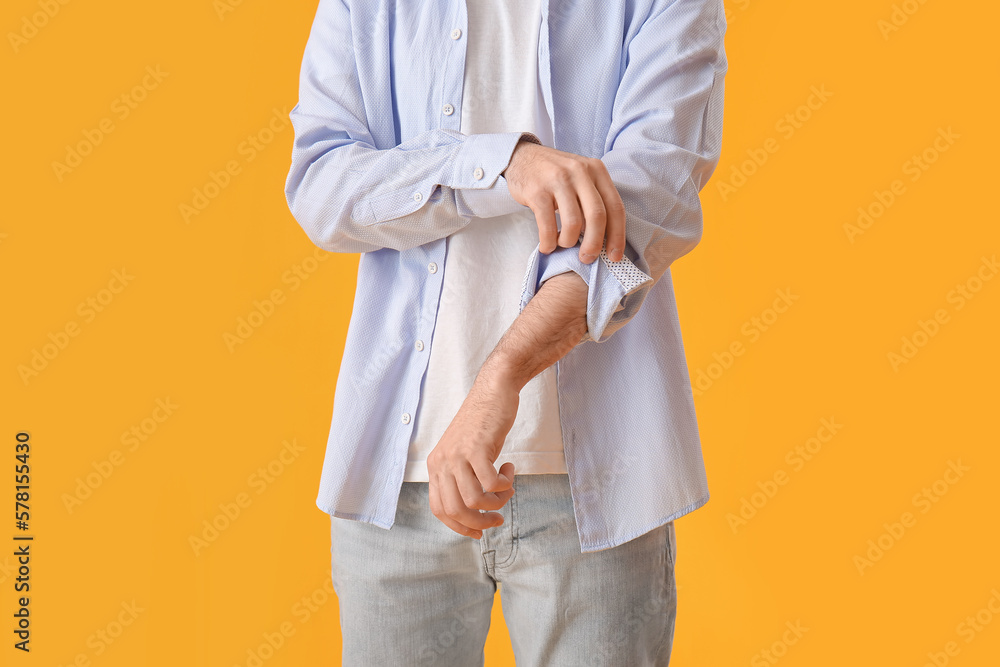 Wall mural Young man rolling up his sleeve on yellow background - Wall murals