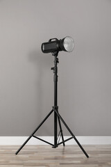 Professional studio flash light with reflector on tripod near grey wall in room. Photography equipment