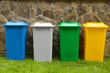 Many colorful recycling bins near stone fence outdoors