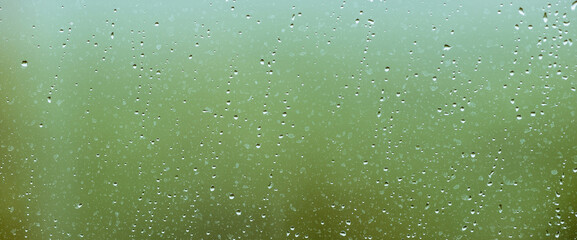 Atmospheric minimal backdrop with rain droplets on glass. Wet window with rainy drops and dirt spots closeup. Blurry minimalist background with greenery bokeh against dirty window glass with raindrops
