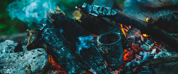 Vivid smoldered firewoods burned in fire close-up. Atmospheric warm background with orange flame of campfire and blue smoke. Wonderful full frame image of bonfire. Burning logs in beautiful fire.