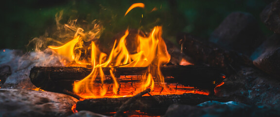 Vivid smoldered firewoods burned in fire close-up. Atmospheric warm background with orange flame of...