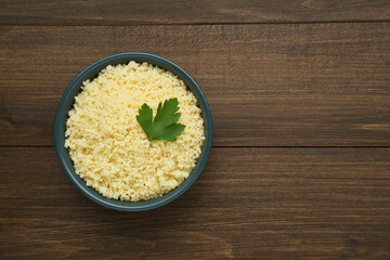 Tasty couscous with parsley on wooden table, top view. Space for text