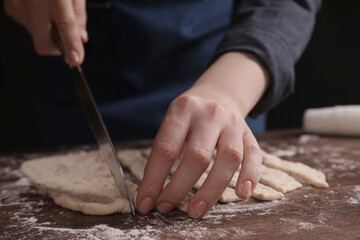 Woman cutting dough at wooden table, closeup. Cooking grissini