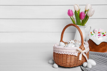 Wicker basket with festively decorated eggs, beautiful tulips and traditional Easter cake on white...