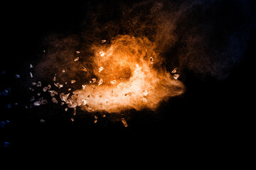 Split debris of stone exploding with orange dust against black background.