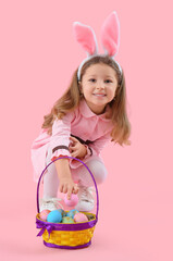 Obraz na płótnie Canvas Cute little girl in bunny ears with basket of Easter eggs on pink background
