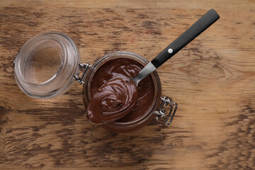 Glass jar and spoon of chocolate paste on wooden table, top view