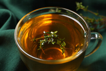 Glass cup of aromatic herbal tea with thyme on green fabric, closeup