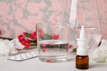 Nasal drops with glass of water on white table. Seasonal allergy concept