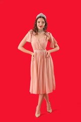 Beautiful young woman in prom dress and tiara on red background