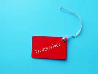 Red luggage tag on blue background  on with handwritten text TRANSCRIBER, means Transcriptionist or...