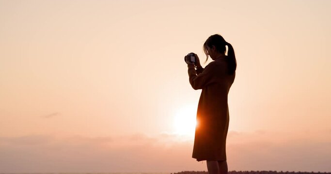 Silhouette of woman use camera to take photo at sunset in the beach