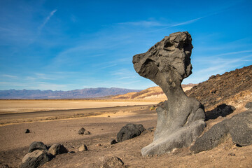 Large natural stone monument overlooks vast desert landscape on clear day with blue sky.