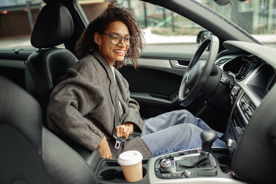 Smiling woman driver in eyeglasses fastens her seat belt before starting car. Driving safety concept