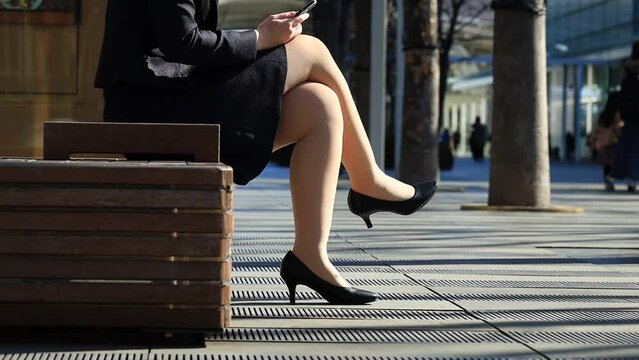 女性　屋外　足を組んでベンチに座っている　ビジネス　イメージ