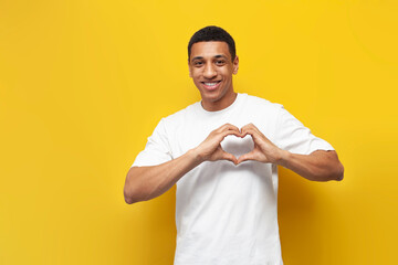 young african american guy in white oversized t-shirt shows heart with his hands, man shows a symbol of love
