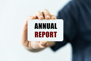 Annual report text on blank business card being held by a woman's hand with blurred background. Business concept about annual report.