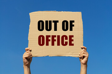 Out of office text on box paper held by 2 hands with isolated blue sky background. This message...