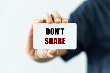 Don't share text on blank business card being held by a woman's hand with blurred background. Business concept to encourage not to share sensitive or fake information.