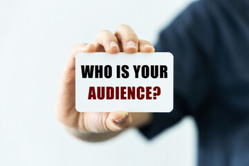 who is your audience text on blank business card being held by a woman's hand with blurred background. Business concept to tell that you should know your audience.