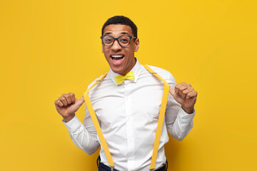 young afro american guy in festive outfit with bow tie and suspenders on yellow isolated...