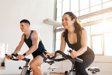 athletic couple of cyclists train on static bicycle simulator, man trainer and fitness woman go in...