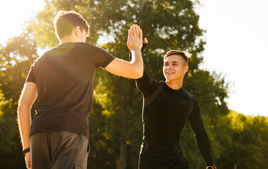 Two athletic men are high five while exercising on mat outdoors. Male friends in sportswear. Healthy lifestyle. Joint training