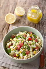 Fresh homemade colorful vegan fusilli pasta salad with beans, corn, tomato, cucumber and green bell pepper served in bowl, photographed on wood (Selective Focus, Focus one third into the image)