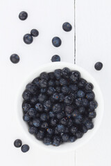 Fresh raw Patagonian Calafate berries (lat. Berberis heterophylla), photographed overhead on white wood (Selective Focus, Focus on the berries in the bowl)