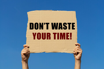 Don't waste your time text on box paper held by 2 hands with isolated blue sky background. This...