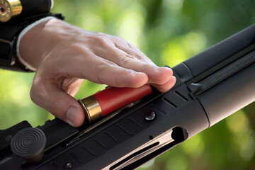 A shotgun shooter is loading a shot into the barrel of a long shotgun.