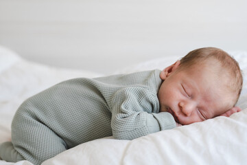 Cute caucasian several days old newborn sleeping on white blanket at home.Adorable,calm, innocent baby indoors.Copy space. Full body shot.Minimalism,lifestyle. Close-up shot