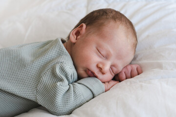 Cute caucasian several days old newborn sleeping on stomach on white blanket at home.Adorable,calm, innocent baby indoors.Copy space. Half body shot.Minimalism,lifestyle, child sweet dreams.