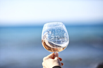 a glass of port wine on the background of the sea, a hand with wine