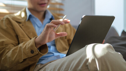 Cropped shot young man sitting in bright living room and using digital tablet.