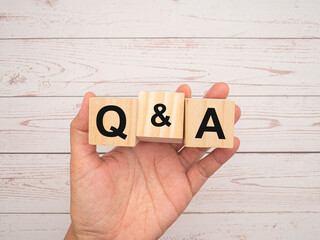 Wooden cubes with the words Q and A in hand over a wooden table