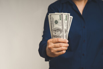 Businessman in a blue shirt holding US dollar bills while standing on a gray background