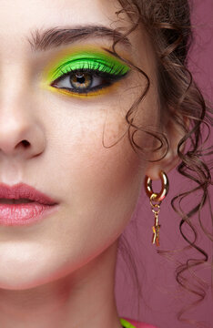 Young woman on pink background with green eyes makeup and curly hair.