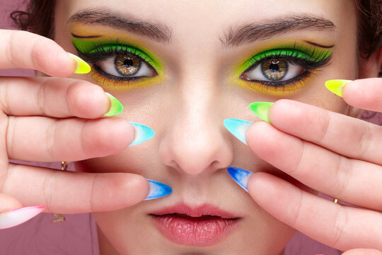 Young woman with green eyes makeup and multi-colored nails manicure.
