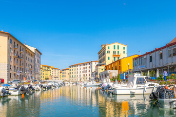 Colorful residential buildings reflect off the water in the boat filled canals at the old port of Livorno, Italy.	 - obrazy, fototapety, plakaty