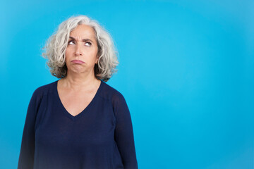 Mature woman looking up with an expression of discontent - obrazy, fototapety, plakaty