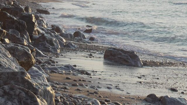 morning sun is reflected on rocky sea coast as waves wash on shore calmly
