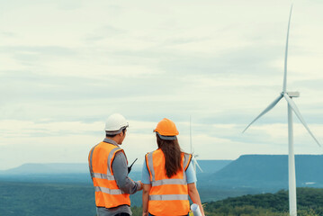 Male and female engineers working on a wind farm atop a hill or mountain in the rural. Progressive ideal for the future production of renewable, sustainable energy. - obrazy, fototapety, plakaty