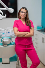Female dentist standing with arms crossed in her office, looking at camera smiling