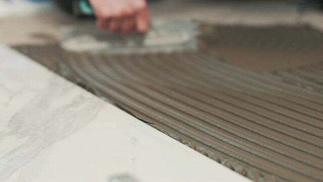 Close up of a worker spreading tile adhesive with a notched trowel. Construction. Renovation.