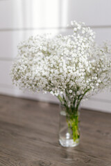 Bouquet of small white flowers in a glass vase in a bright sunny interior. White gypsophila close-up.