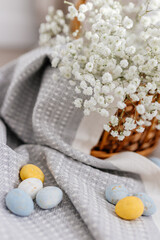 A wicker brown basket, inside which, on a gray linen napkin, are painted yellow, blue, white eggs and white small flowers.  Spring background for Easter. Mock up. Space for text