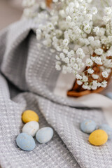 A wicker brown basket, inside which, on a gray linen napkin, are painted yellow, blue, white eggs and white small flowers.  Spring background for Easter. Mock up. Space for text