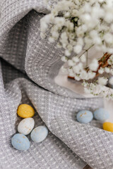 A wicker brown basket, inside which, on a gray linen napkin, are painted yellow, blue, white eggs and white small flowers.  Spring background for Easter. Mock up. Space for text